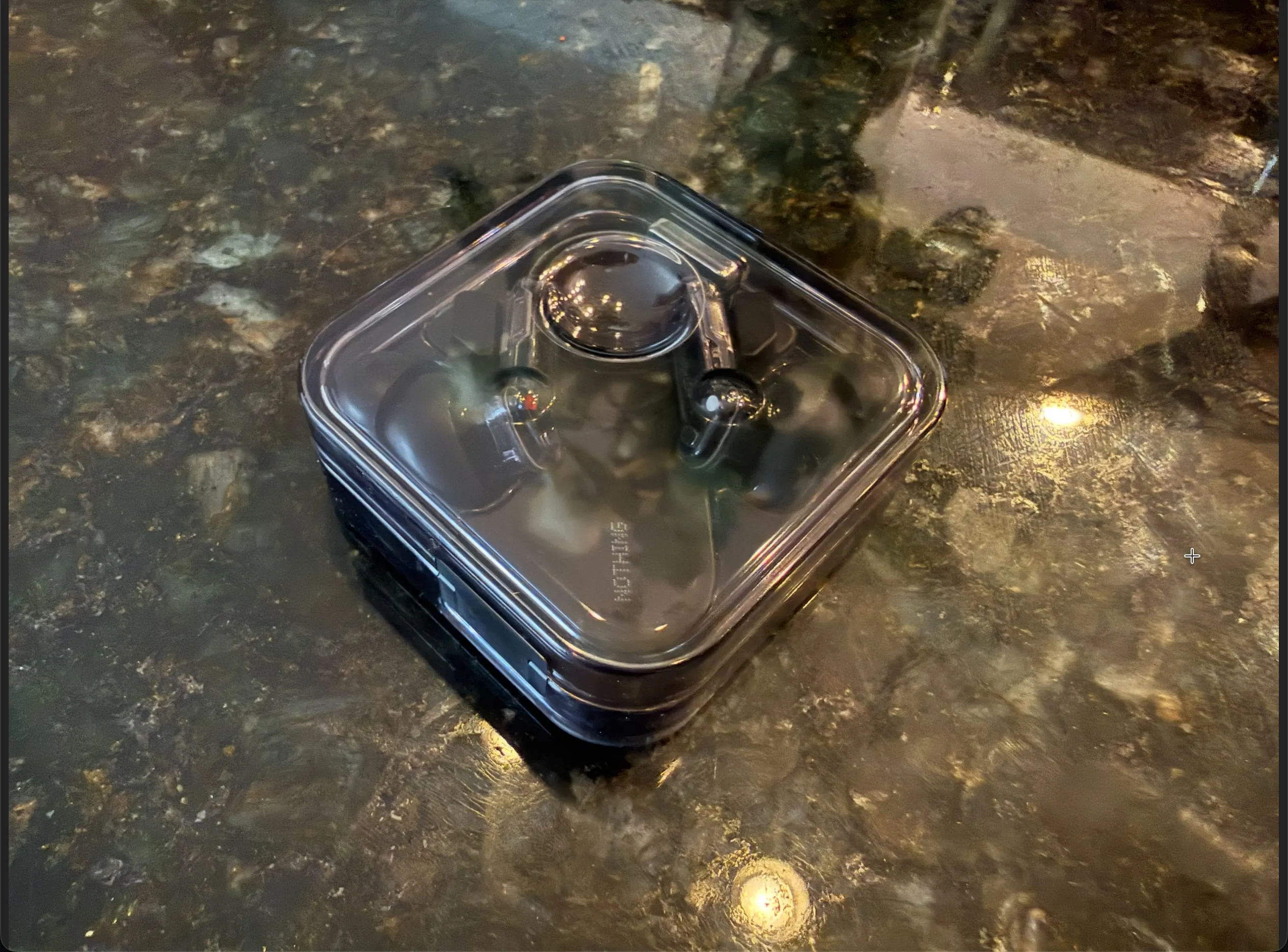 The closed transparent Nothing Ear (2024) case on a dark stone counter.