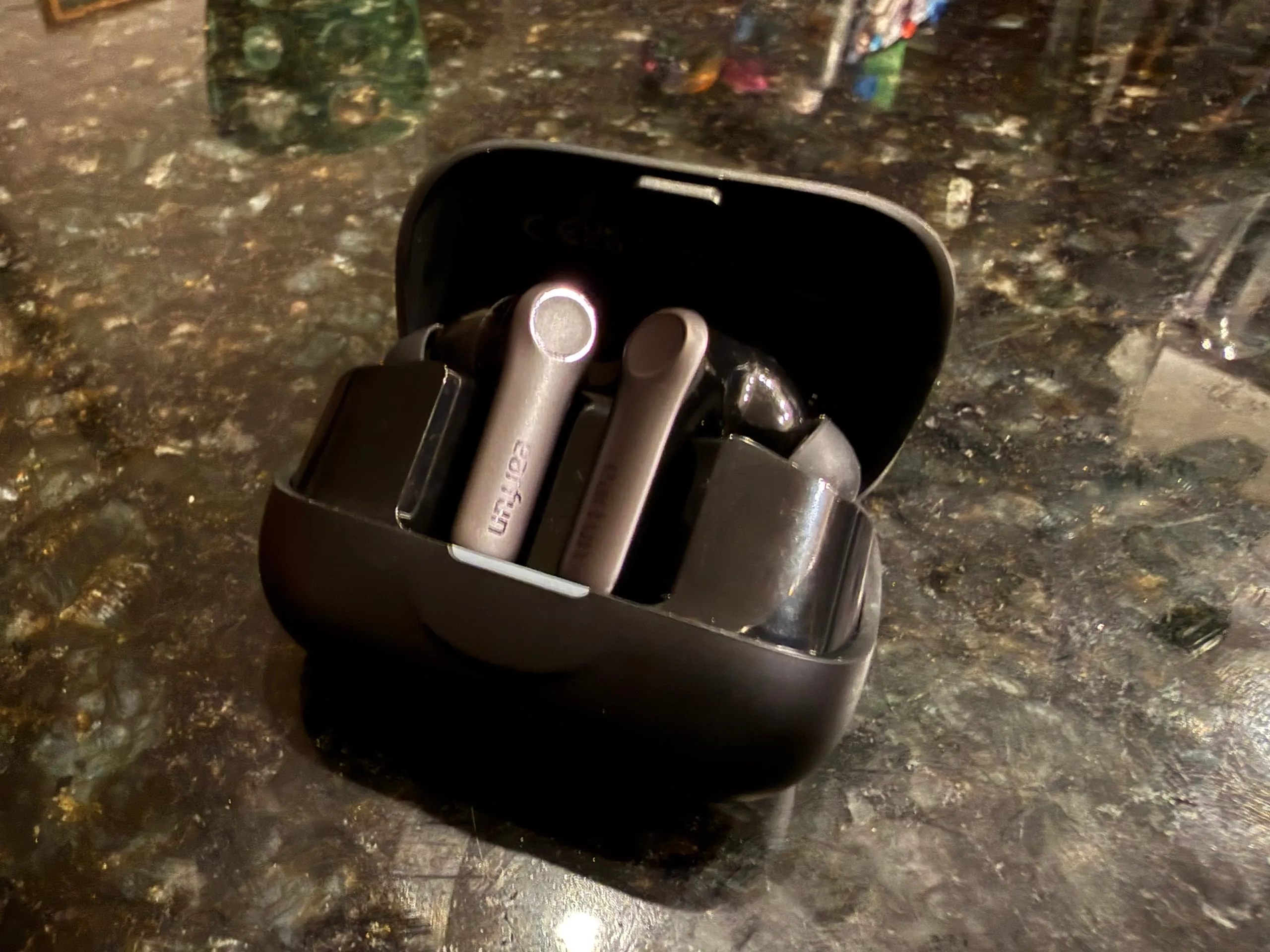 The EarFun Air Pro 4+ in its open black case on a dark stone counter, both buds seated stem-up.